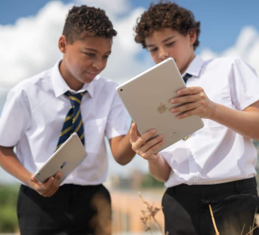 Two young male pupils using their iPad devices outdoors for one of their lessons.